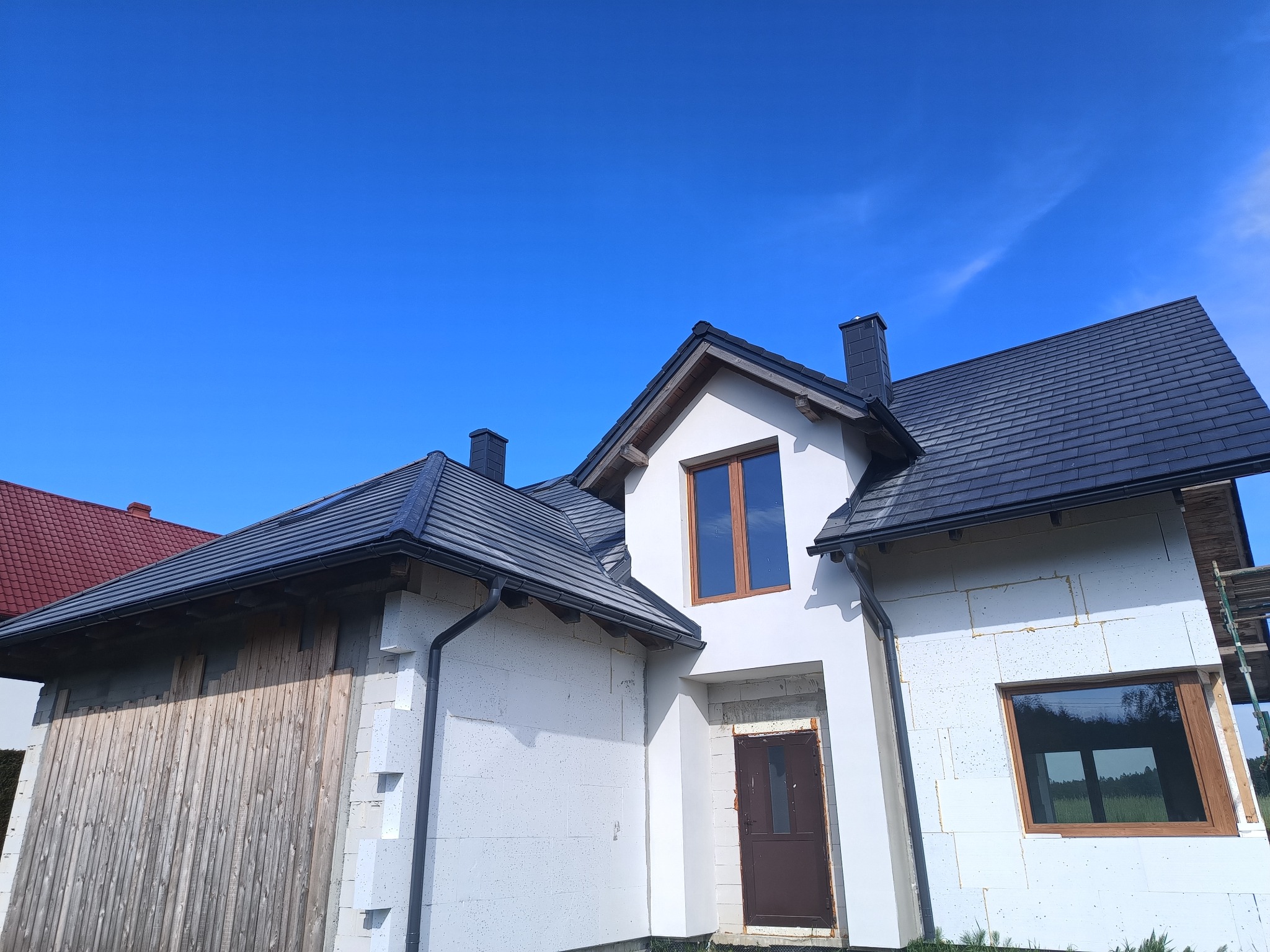 Nowy dach z grafitowej dachówki ceramicznej na budynku w trakcie budowy, widoczne rynny i obróbki blacharskie, styropianowe ocieplenie ścian.