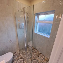 Szymon - Nowoczesna łazienka po remoncie: kabina prysznicowa ze szklaną ścianką, ozdobne płytki podłogowe z motywem geometrycznym, ściany wyłożone pionowymi, jasnymi płytkami imitującymi cegłę, okno...