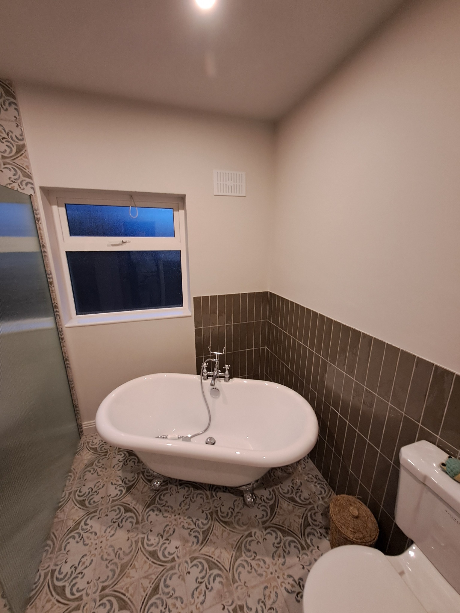 Wykończona łazienka z wolnostojącą wanną na nóżkach, wzorzystą podłogą i ciemnymi płytkami do połowy ściany, widok z góry.