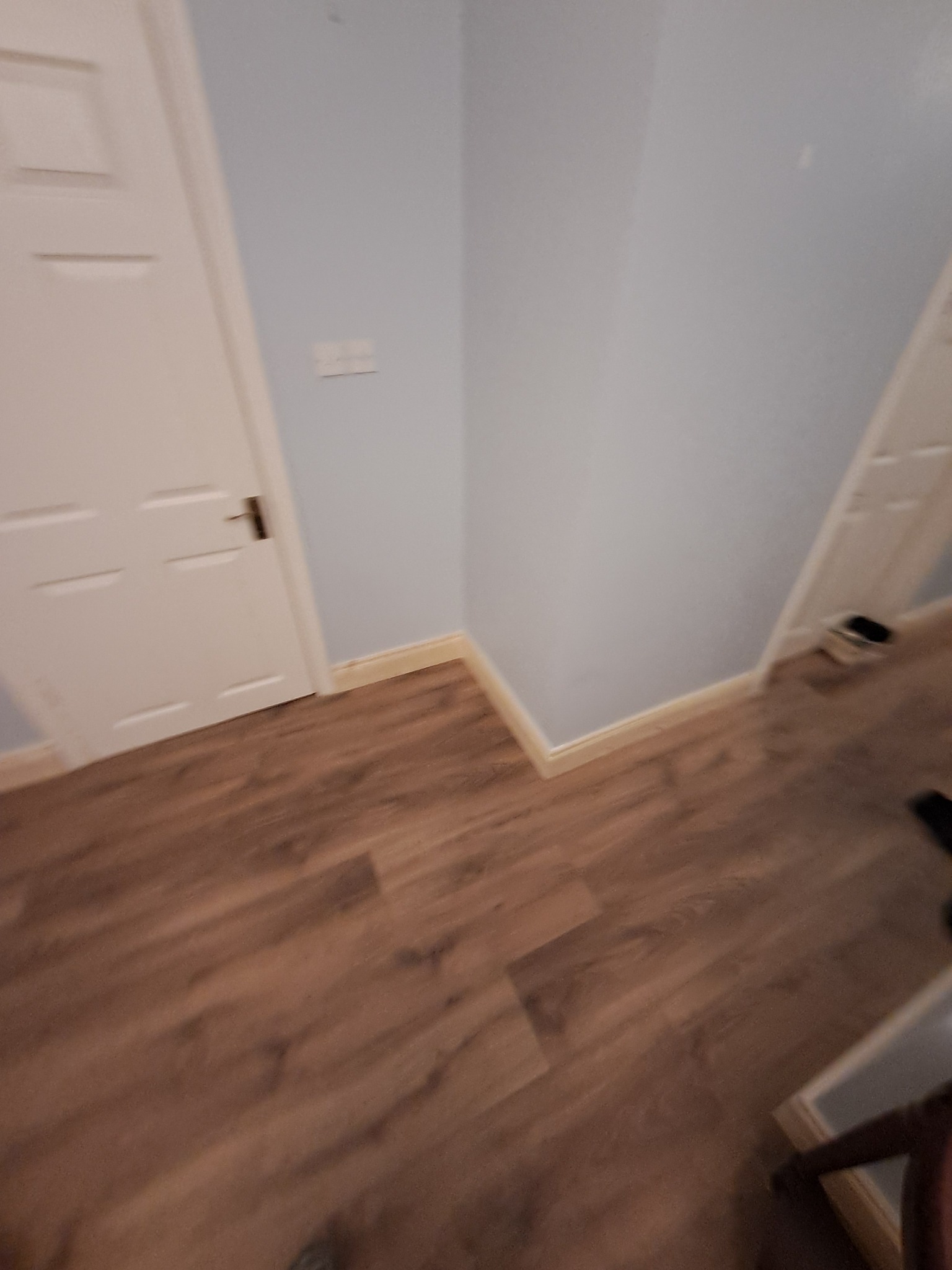 Fragment pokoju po ułożeniu paneli podłogowych w odcieniach brązu, z widoczną białą listwą przypodłogową i białymi drzwiami.