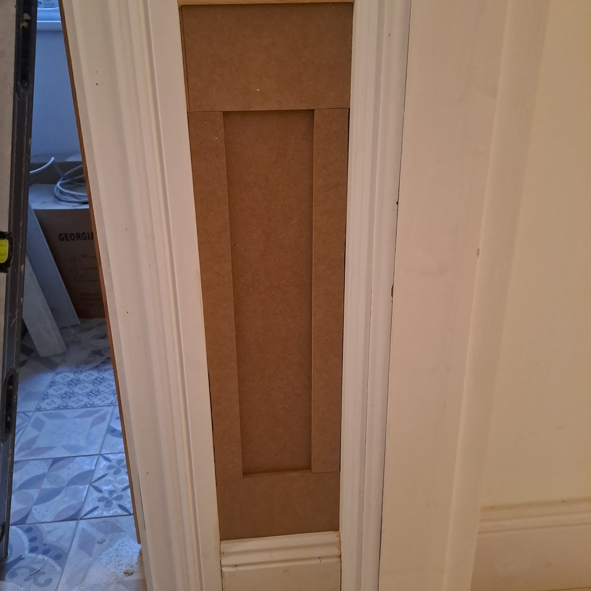 Fragment ościeżnicy drzwiowej z zamontowaną płytą MDF, widoczne ślady po szpachlowaniu i poziomica w tle.