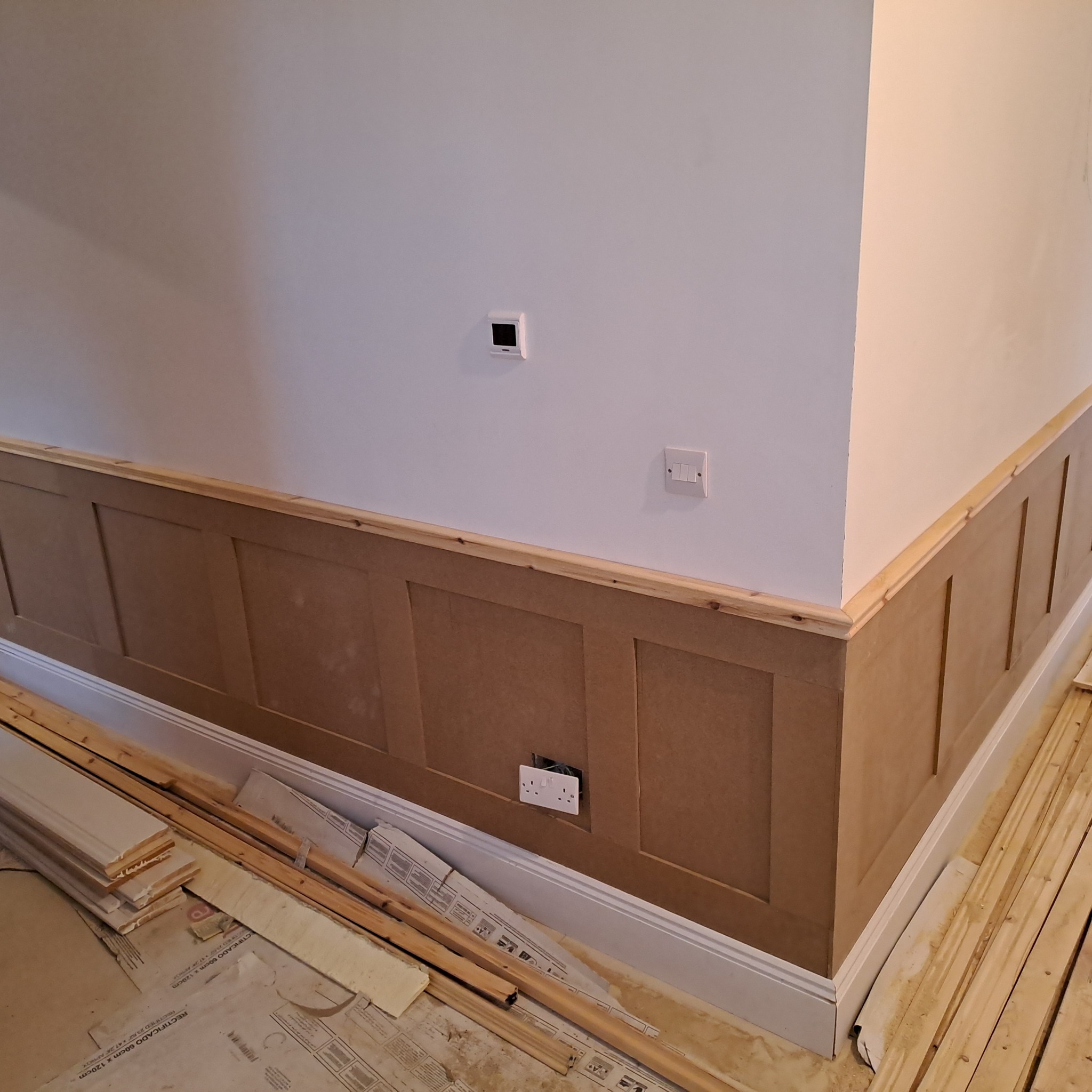 Montaż paneli ściennych MDF w trakcie realizacji, widoczne listwy przypodłogowe, gniazdko elektryczne i elementy konstrukcyjne na podłodze.