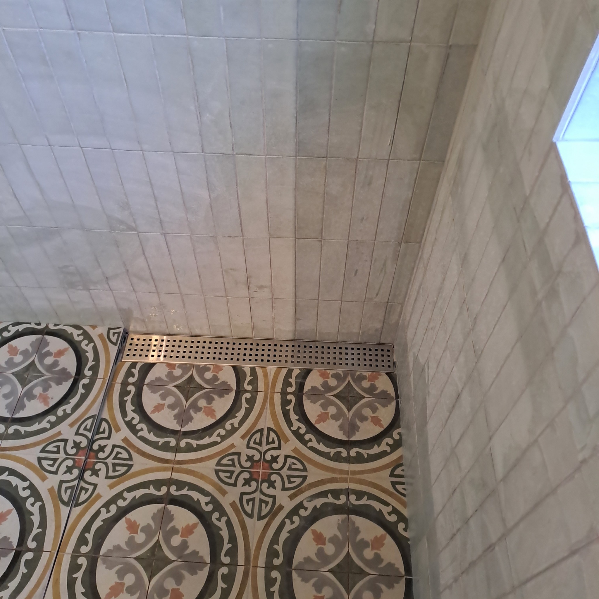 Wykończona łazienka z ozdobnymi płytkami podłogowymi w stylu retro, szarymi płytkami ściennymi ułożonymi pionowo i odpływem liniowym.