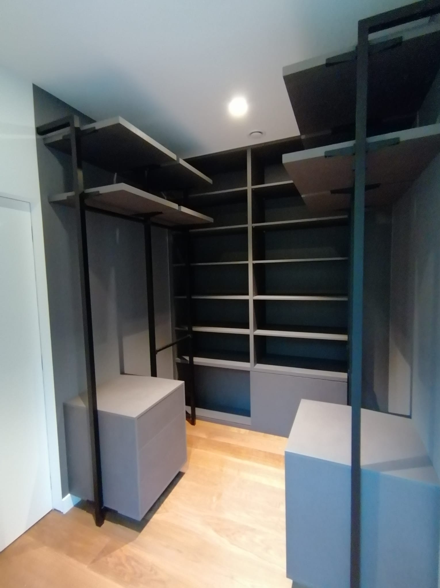 Nowoczesna garderoba z otwartymi półkami i szufladami w odcieniach szarości, z drewnianą podłogą, minimalistyczny design.