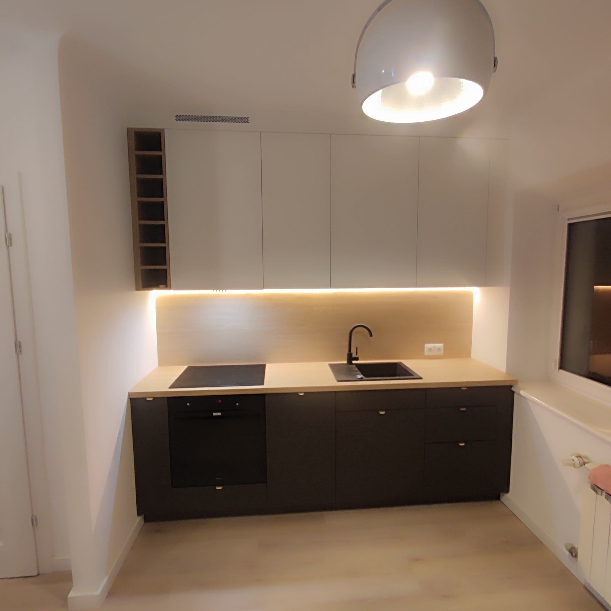 Nowoczesna kuchnia z białymi szafkami górnymi i ciemnymi dolnymi, oświetleniem LED pod szafkami, czarnym zlewem i płytą indukcyjną, zlokalizowana w Warszawie.