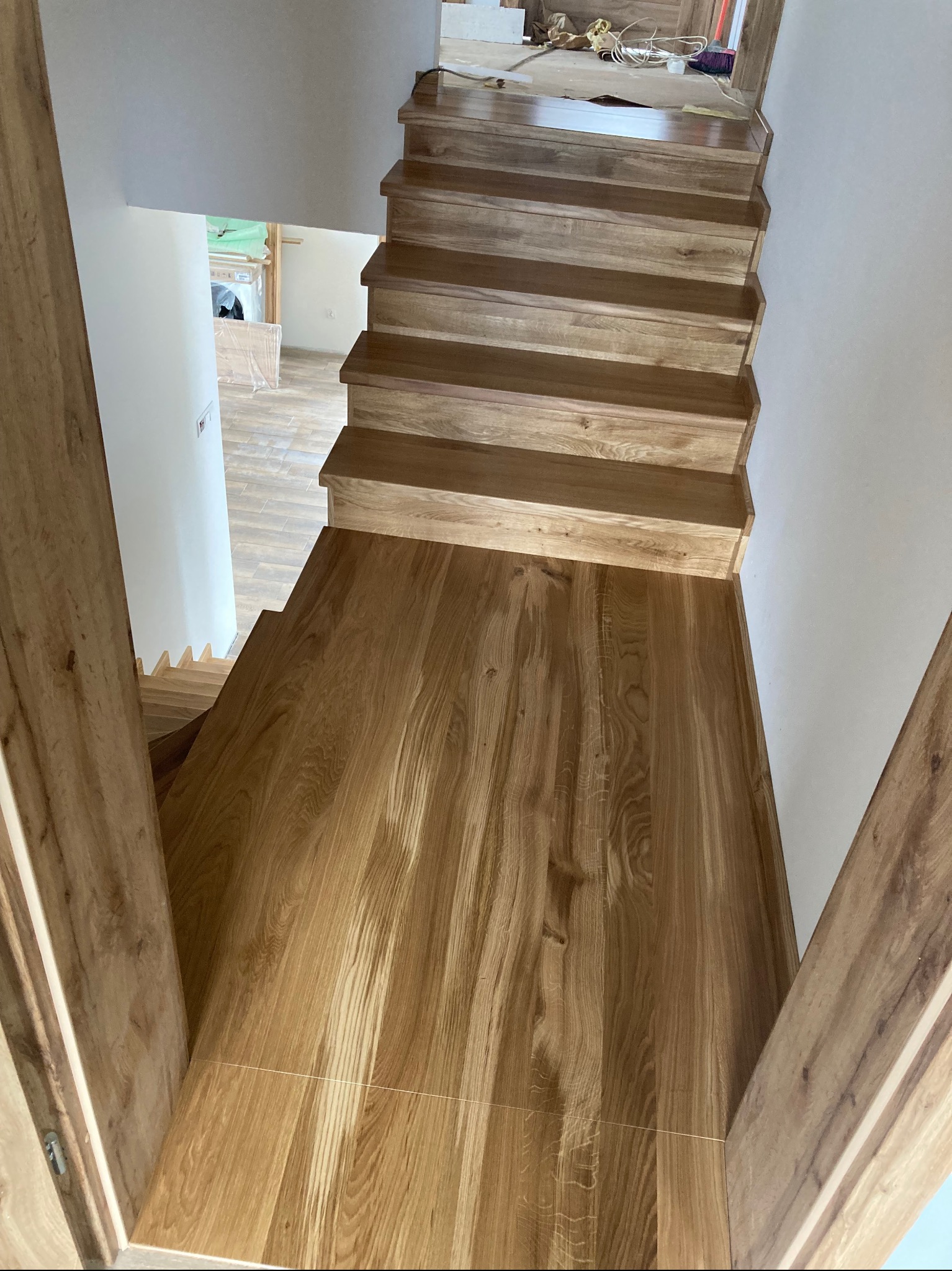 Widok z góry na nowo zamontowane, jasne, drewniane schody w trakcie wykańczania, z widocznymi śladami prac na górnym podeście i w tle.
