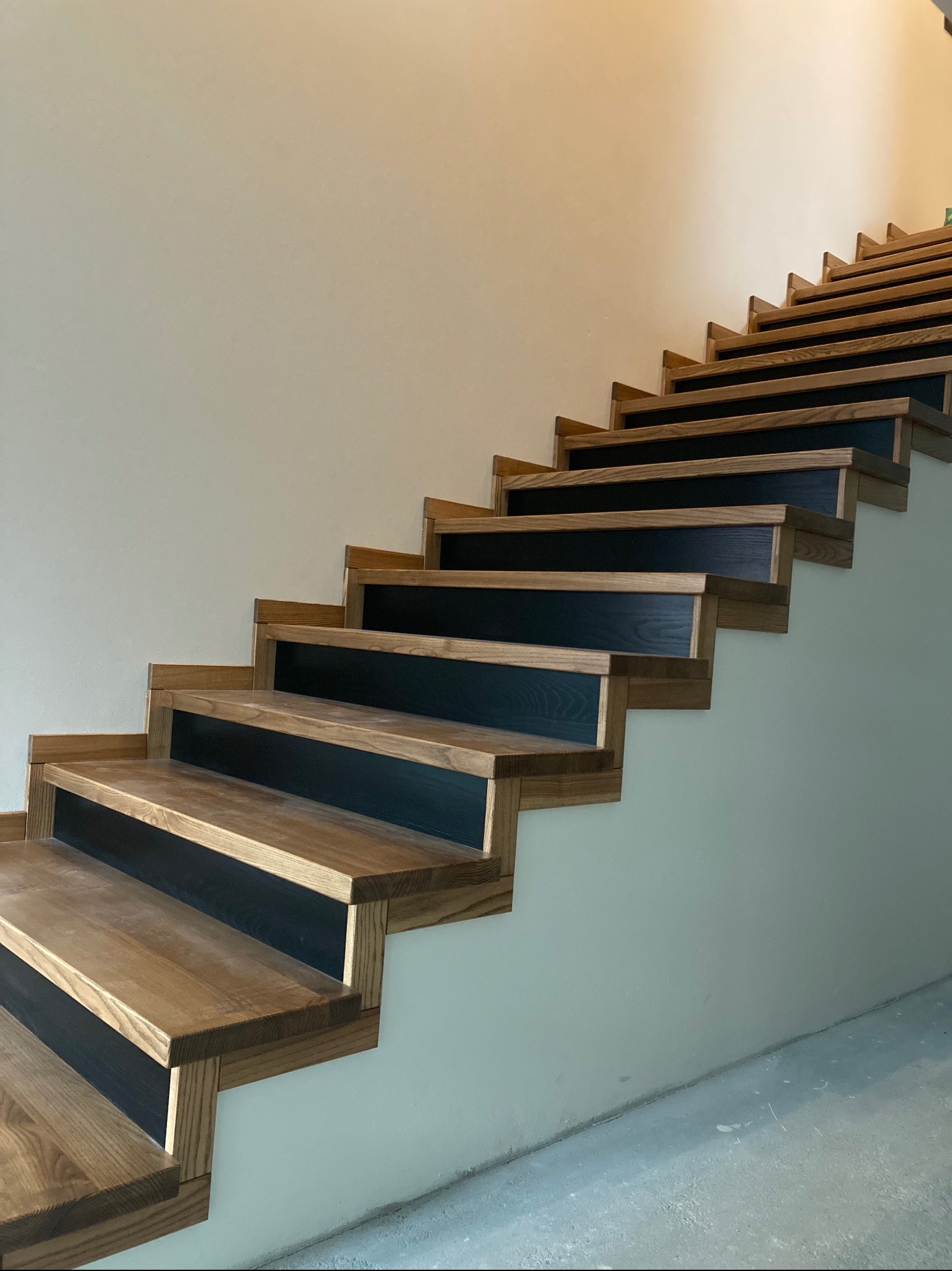 Nowoczesne schody z drewna dębowego z czarnymi podstopnicami, widok z dołu, oświetlone naturalnym światłem. Minimalistyczny design.