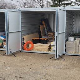 Miejski Box - Rząd otwartych, srebrnych kontenerów magazynowych wypełnionych materiałami budowlanymi, takimi jak drewno, farby, cement i narzędzia.