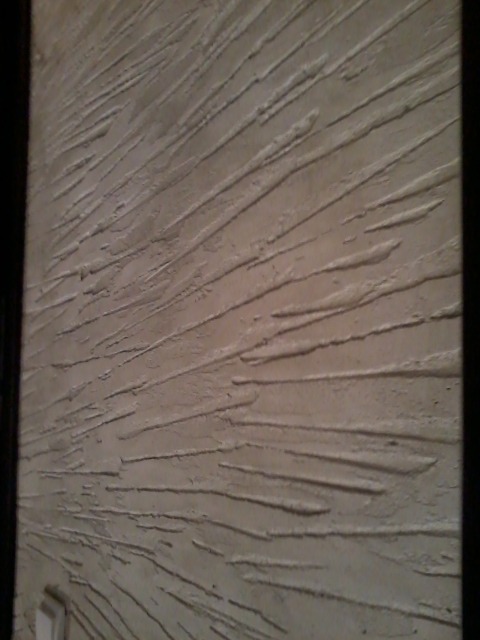 Beżowa ściana z dekoracyjną fakturą w postaci poziomych, wystających linii, tworzących efekt trójwymiarowości.