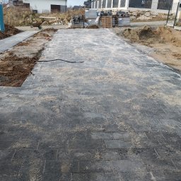 Sebastian Dobrowolski - Ułożona, szara kostka brukowa na posesji w Gryfowie Śląskim. Widoczne palety z kostką, przygotowane podłoże i tymczasowa toaleta. Całość w dziennym oświetleniu.