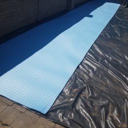 Kamil Perczak - Rozłożone płyty izolacyjne z niebieskiego styropianu z siatką na czarnej folii budowlanej, przygotowanie do ocieplenia poddasza.