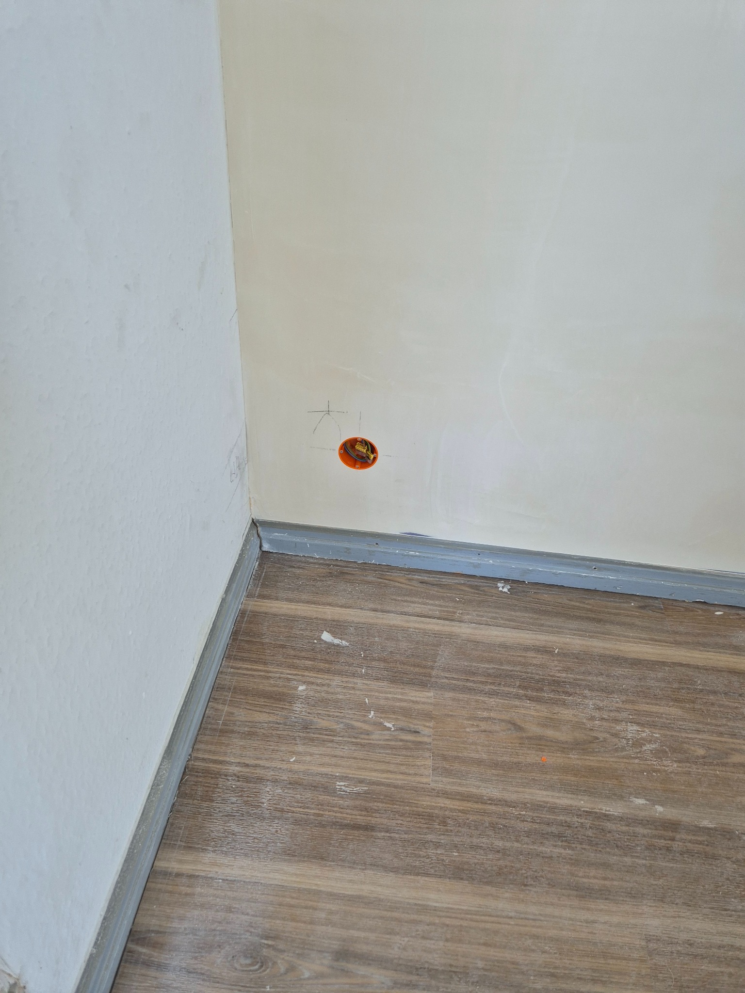 Fragment pokoju w Bydgoszczy w trakcie prac wykończeniowych: ściany po szpachlowaniu, widoczna puszka elektryczna z zaznaczonymi punktami, listwy przypodłogowe i panele podłogowe z drobnymi...