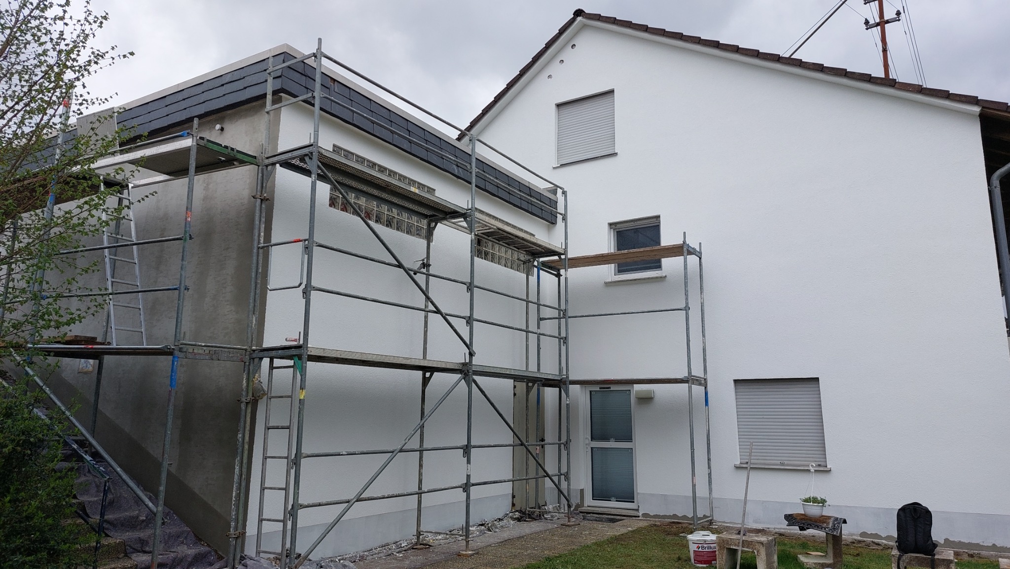 Dom w trakcie malowania elewacji, widoczne rusztowania, fragment elewacji w stanie surowym i pomalowanym na biało, okna z roletami.