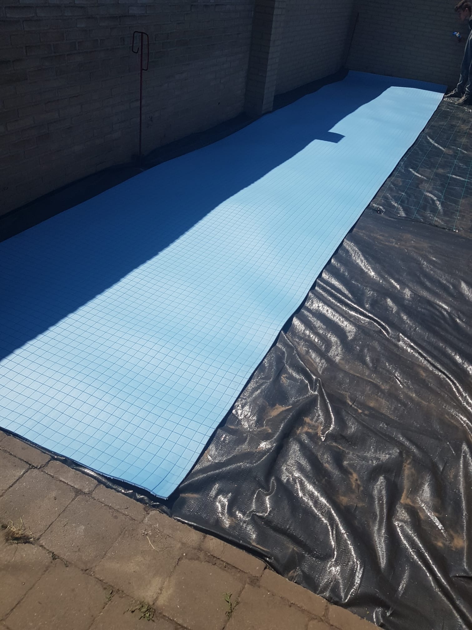 Rozłożone płyty izolacyjne z niebieskiego styropianu z siatką na czarnej folii budowlanej, przygotowanie do ocieplenia poddasza.