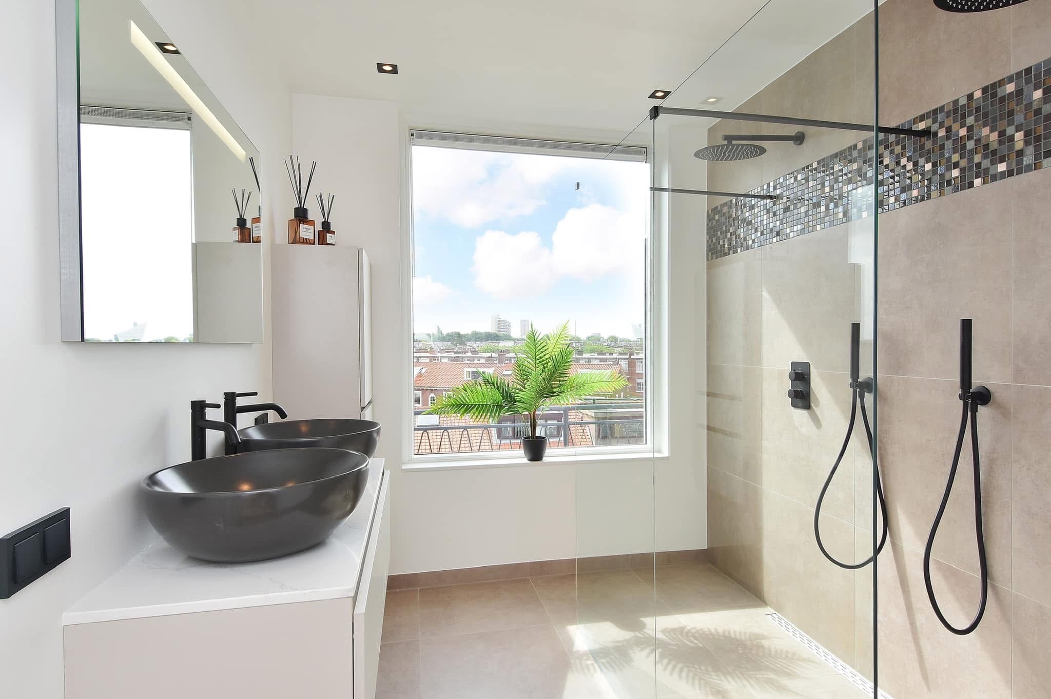 Nowoczesna łazienka z kabiną prysznicową typu walk-in, dwiema umywalkami w kolorze antracytowym i widokiem na miasto z okna.