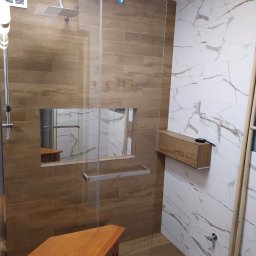 Jurek-PROF - Nowoczesna kabina prysznicowa typu walk-in z drewnopodobnymi płytkami, wbudowaną półką wewnątrz i marmurowymi płytkami na sąsiedniej ścianie, uzupełniona o drewnianą szafkę pod umywalkę i dodatkową...