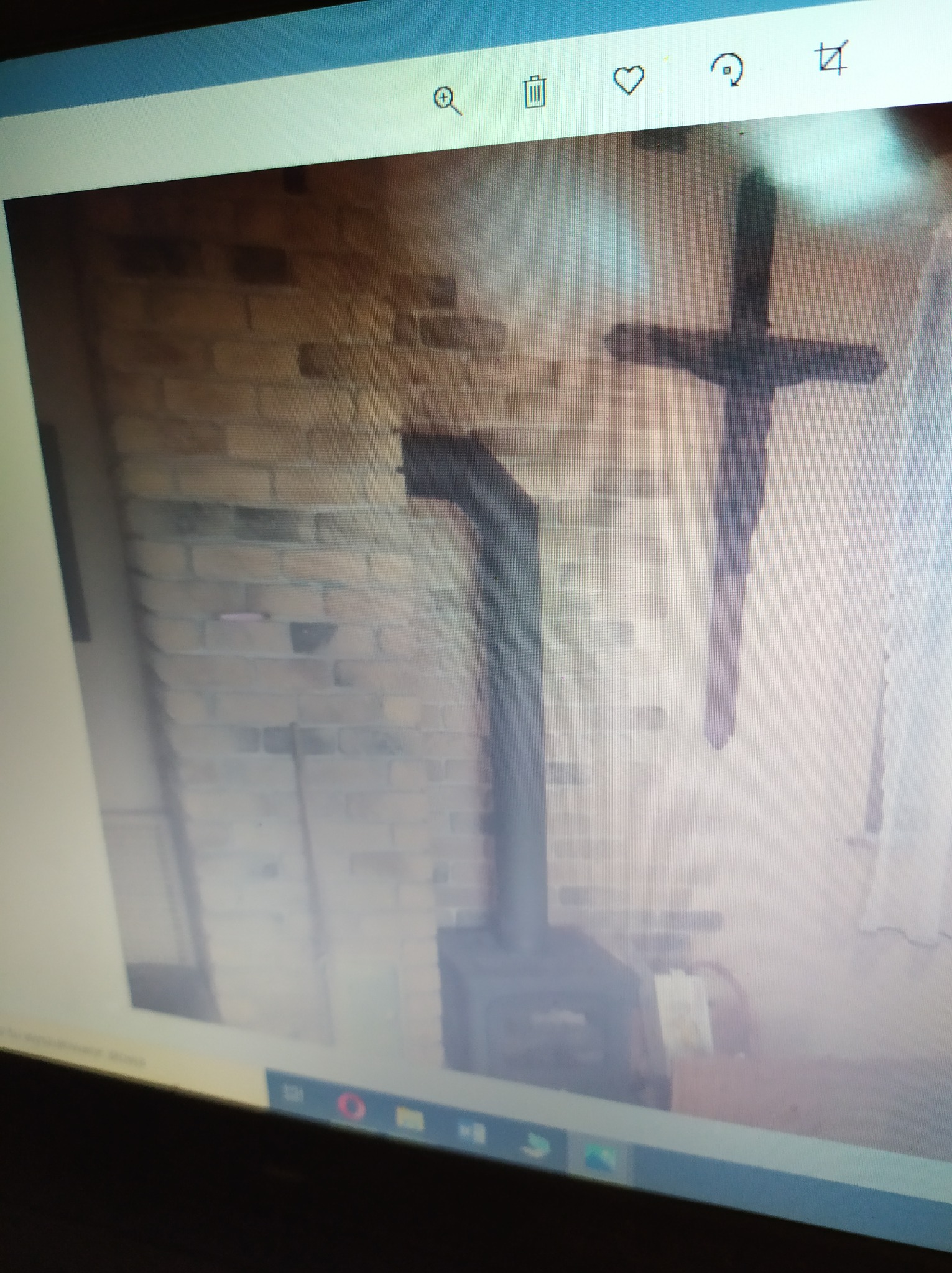 Murowany kominek z czarną rurą odprowadzającą dym, krzyż na ścianie, ujęcie z ekranu komputera.