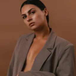 Portret kobiety w brązowym oversize'owym żakiecie na jednolitym tle w Poznaniu, z mocnym makijażem, skierowanej wprost do obiektywu.