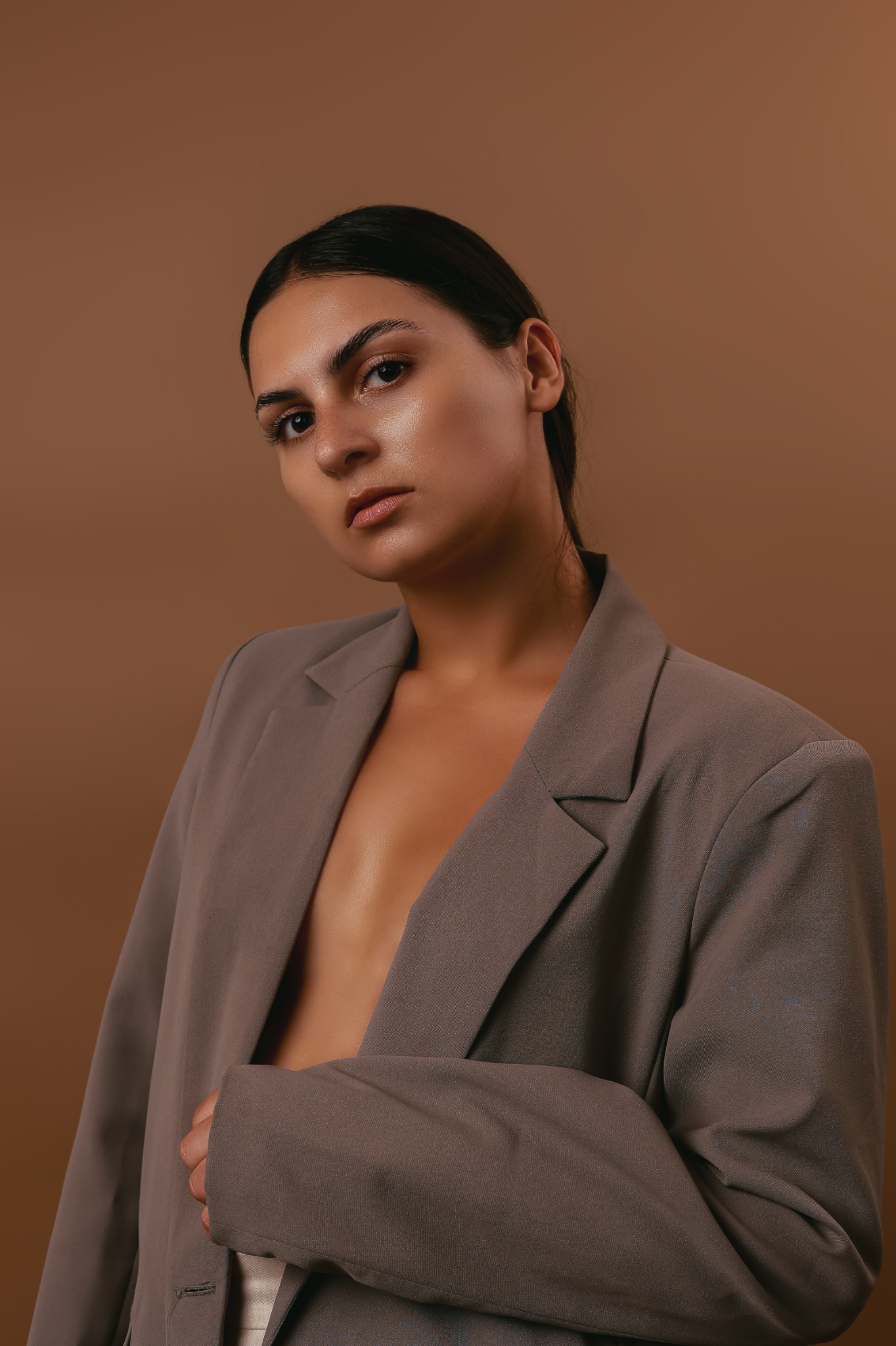 Portret kobiety w brązowym oversize'owym żakiecie na jednolitym tle w Poznaniu, z mocnym makijażem, skierowanej wprost do obiektywu.