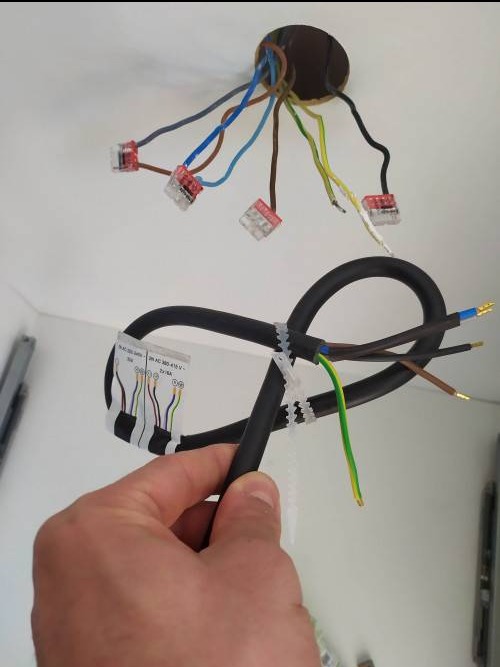 Podłączenie przewodów elektrycznych do puszki sufitowej za pomocą złączek Wago, widoczny kabel z opisem technicznym przymocowany opaskami zaciskowymi.