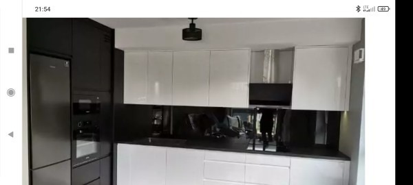 Nowoczesna kuchnia z białymi błyszczącymi szafkami górnymi i dolnymi, czarnym blatem i panelem nad blatem, oraz czarnymi szafkami bocznymi z wbudowanym sprzętem AGD.