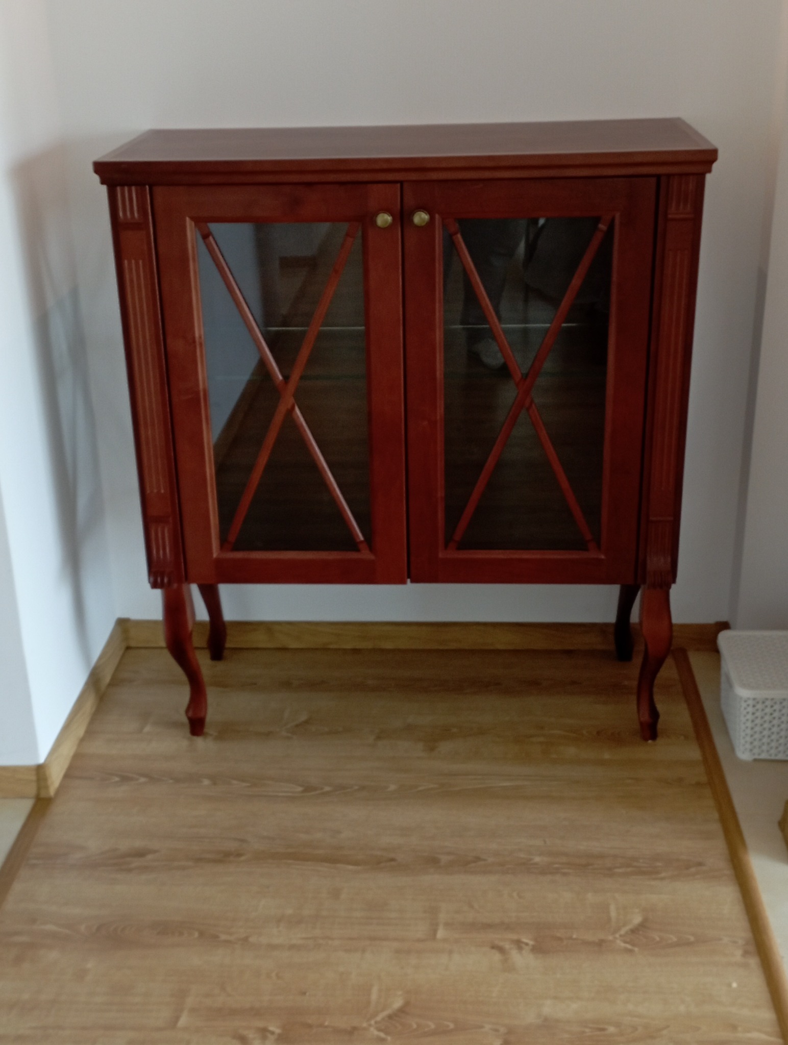 Ręcznie wykonana, drewniana witryna z przeszkleniami w kształcie rombów, na giętych nóżkach, ustawiona na panelach podłogowych. Klasyczny styl.