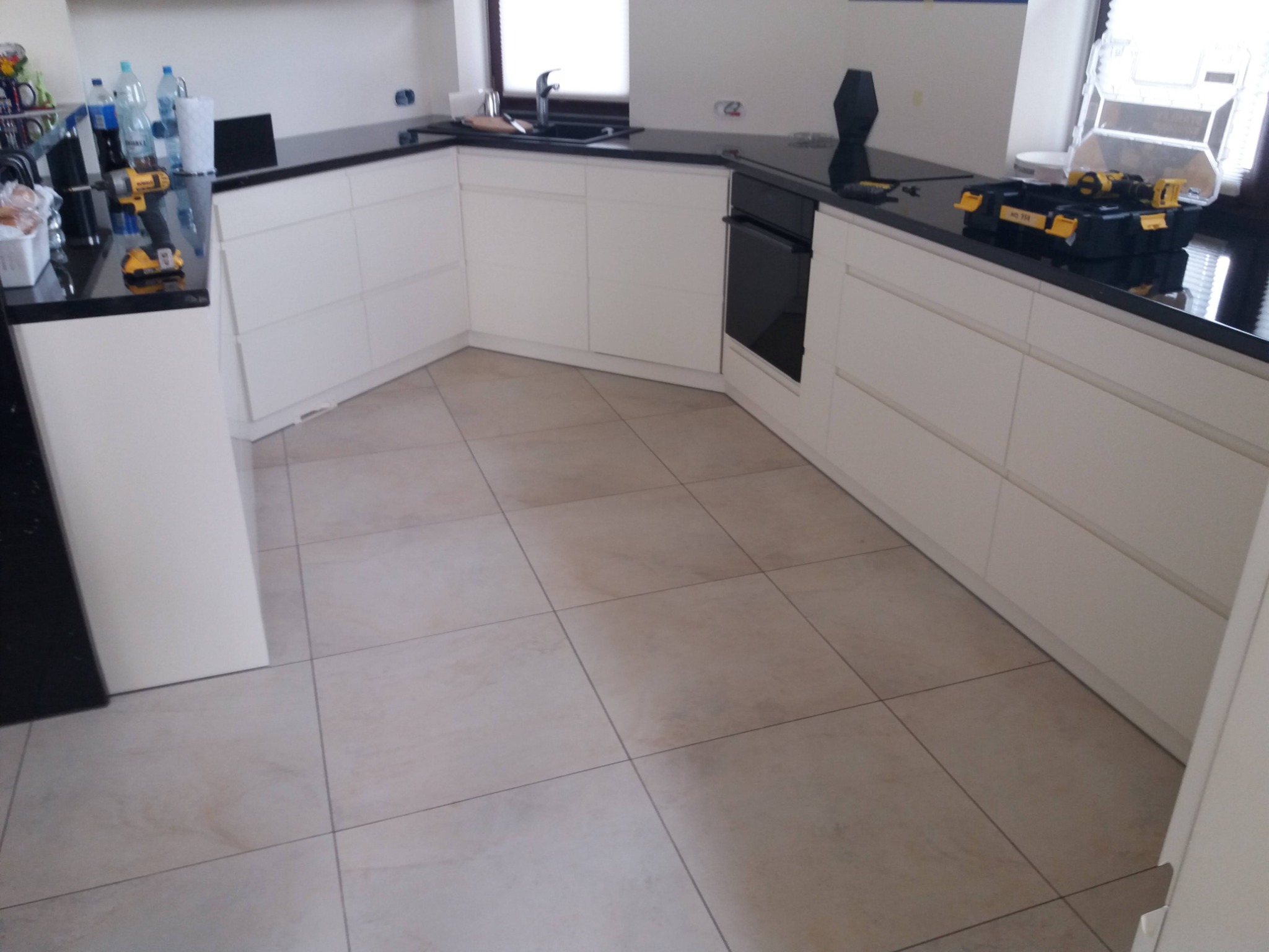 Biała kuchnia z czarnym blatem, widoczne narzędzia montażowe. Ułożona płytki podłogowe. Nowoczesny design, jasne wnętrze.