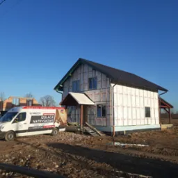 Dom w trakcie budowy, zabezpieczony membraną Tyvek, z zaparkowanym obok vanem z reklamą izolacji natryskowych.