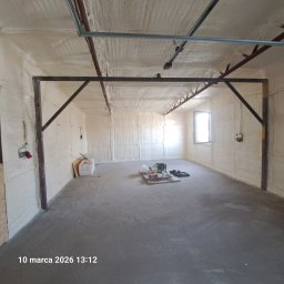 GAWEŁCZYK IZOLACJE NATRYSKOWE - Wnętrze garażu po ociepleniu pianką PUR: ściany i sufit pokryte grubą warstwą izolacji, widoczne metalowe elementy konstrukcyjne i okno w oddali.