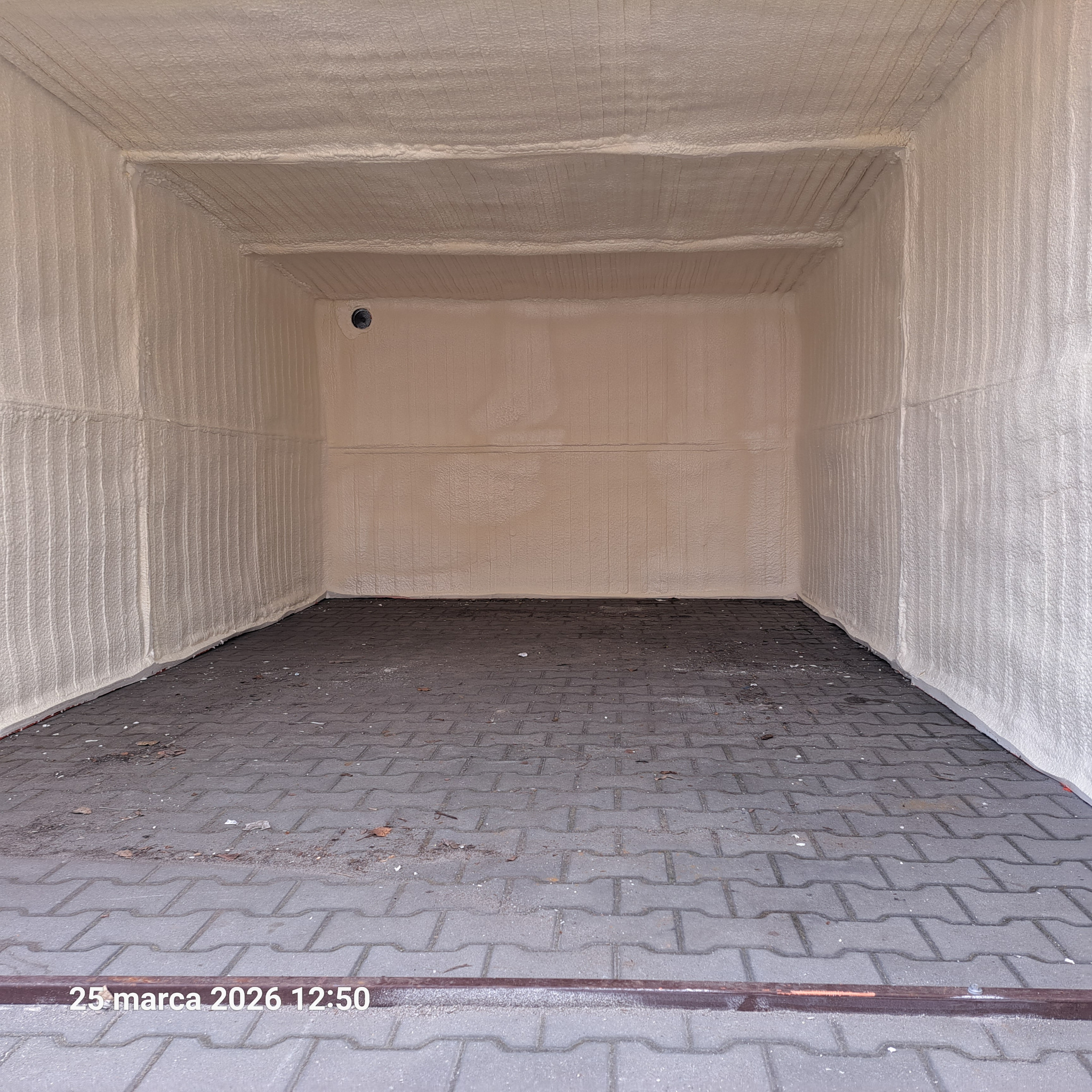 Wnętrze kontenera po ociepleniu pianką PUR, widoczne ściany i sufit pokryte grubą warstwą izolacji. Na podłodze kostka brukowa. Widoczny otwór wentylacyjny.