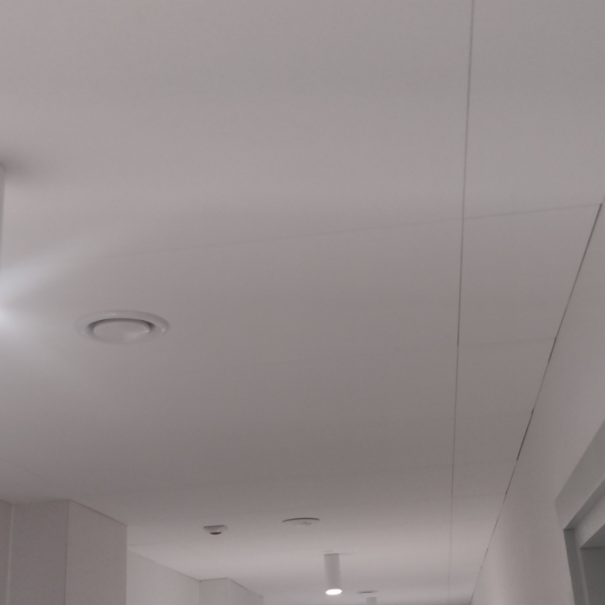 Biały sufit z zamontowanymi panelami gipsowo-kartonowymi, widoczne łączenia i okrągły nawiewnik wentylacyjny w centralnej części kadru.