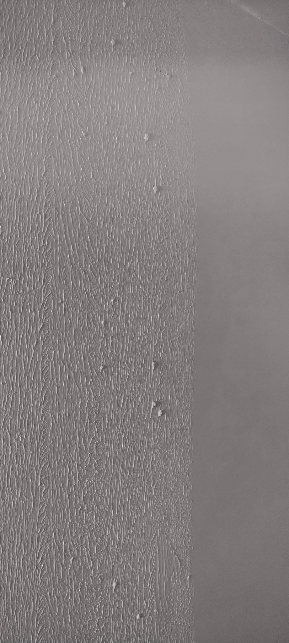 Świeżo nałożona, szara warstwa wykończeniowa z widocznymi śladami pędzla i nierównościami, przylegająca do gładkiej, pomalowanej powierzchni ściany.