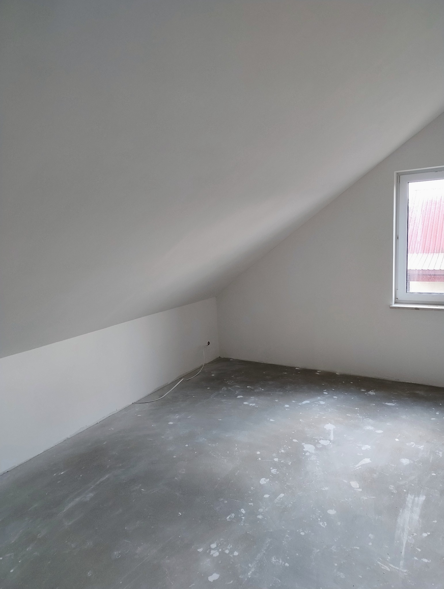 Pokój na poddaszu po szpachlowaniu, przygotowany do dalszych prac wykończeniowych. Widoczne ślady po gładzi na podłodze i świeżo wyszpachlowane ściany.