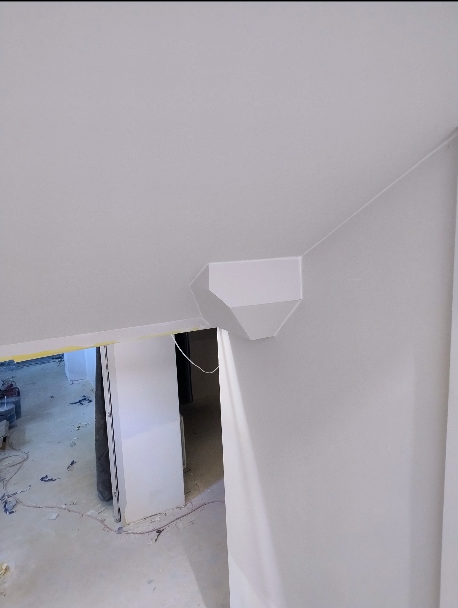 Białe, pomalowane wnętrze z dekoracyjnym elementem na ścianie, widok z dołu. Widoczne wykończenie sufitu i fragment podłogi w trakcie prac.