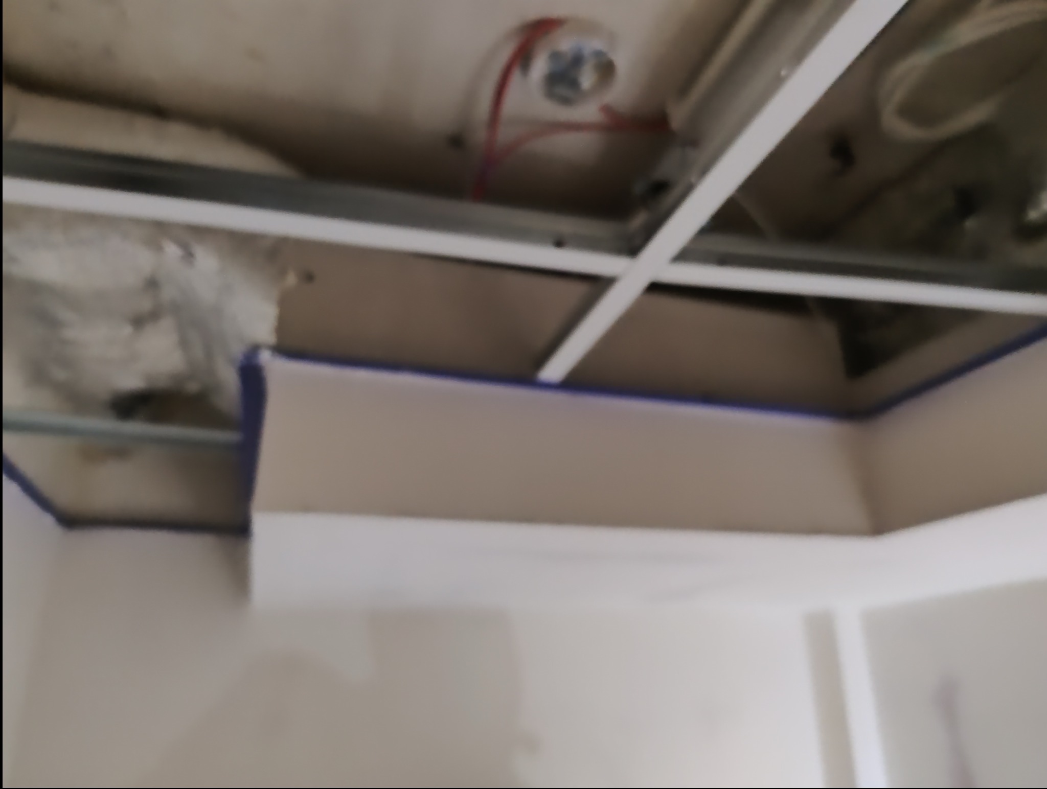 Przygotowanie do malowania: ściany zabezpieczone taśmą malarską, widoczna konstrukcja sufitu podwieszanego i instalacja elektryczna w tle. Prace wykończeniowe.