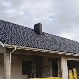 Daniel Wołoszyn - Nowy, czarny dach z ceramicznej dachówki karpiówki i jasne rynny na surowym budynku z betonu komórkowego. Widoczny komin i zapakowane bloczki Ytong.