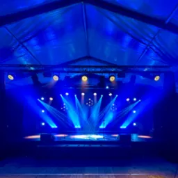 Scena oświetlona niebieskimi światłami, z mikrofonami i kolumnami. Oświetlenie sceniczne w namiocie eventowym, tworzące unikalny klimat imprezy.