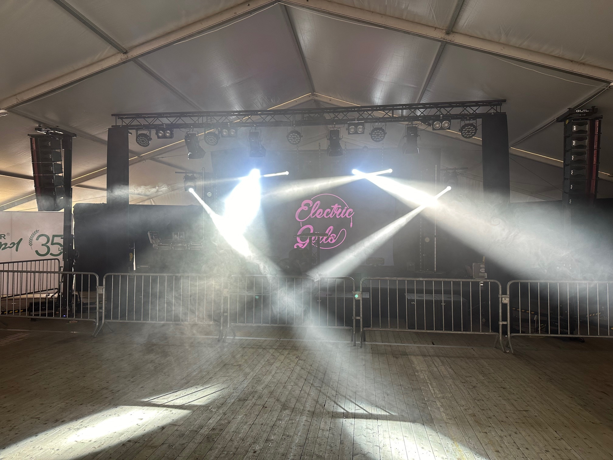 Scena oświetlona reflektorami i wypełniona dymem, z widocznym nagłośnieniem, pod zadaszeniem namiotu.