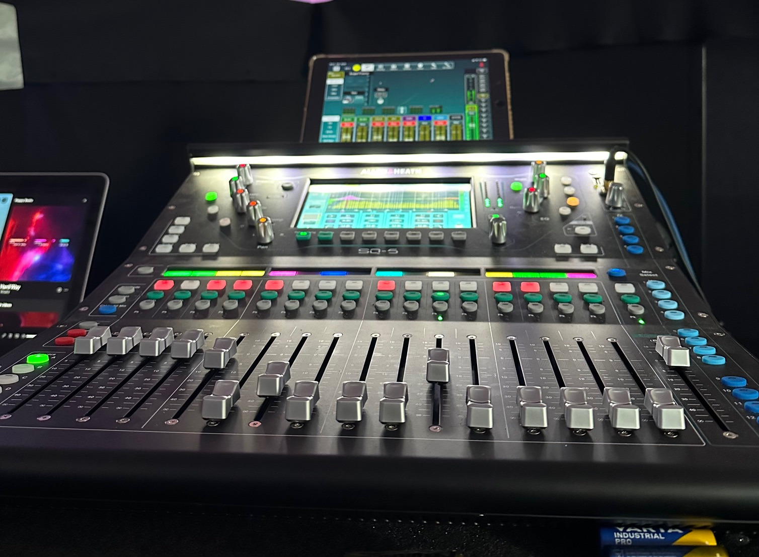 Czarny mikser cyfrowy Allen&Heath SQ-5 z podświetlonymi przyciskami i suwakami, widoczne dwa tablety z aplikacjami do sterowania dźwiękiem w tle.