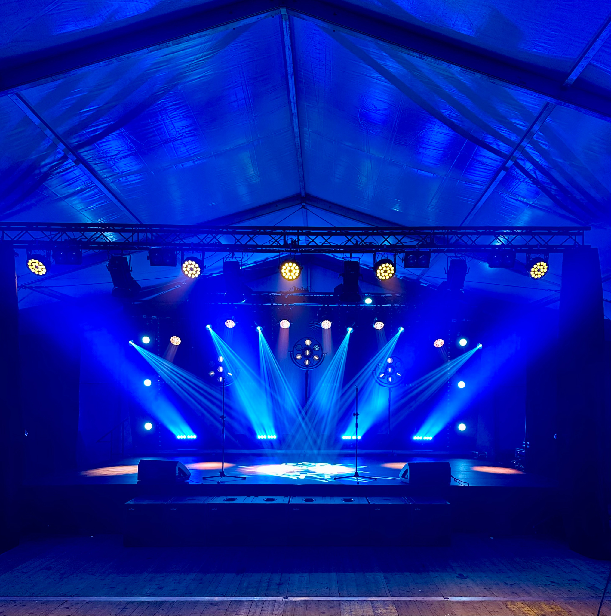 Scena oświetlona niebieskimi światłami, z mikrofonami i kolumnami. Oświetlenie sceniczne w namiocie eventowym, tworzące unikalny klimat imprezy.