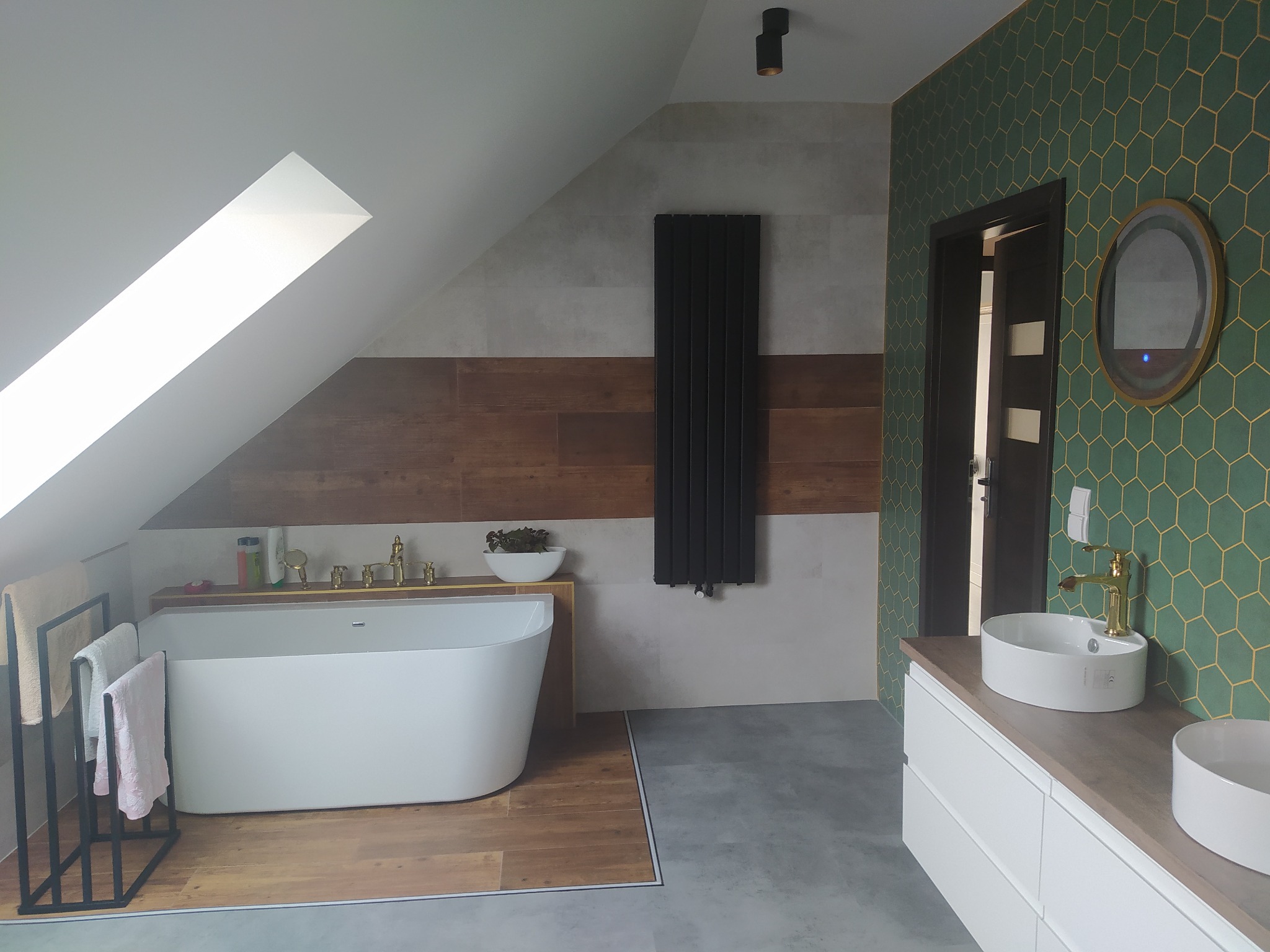 Nowoczesna łazienka na poddaszu z wanną wolnostojącą, umywalkami nablatowymi i zieloną ścianą w geometryczny wzór. Uwagę zwraca oryginalne oświetlenie i aranżacja.