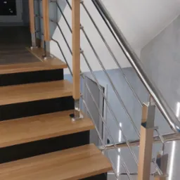 Schody z drewnianymi stopniami i balustradą ze stali nierdzewnej z drewnianymi słupkami, widok z dołu na górę, nowoczesny design.