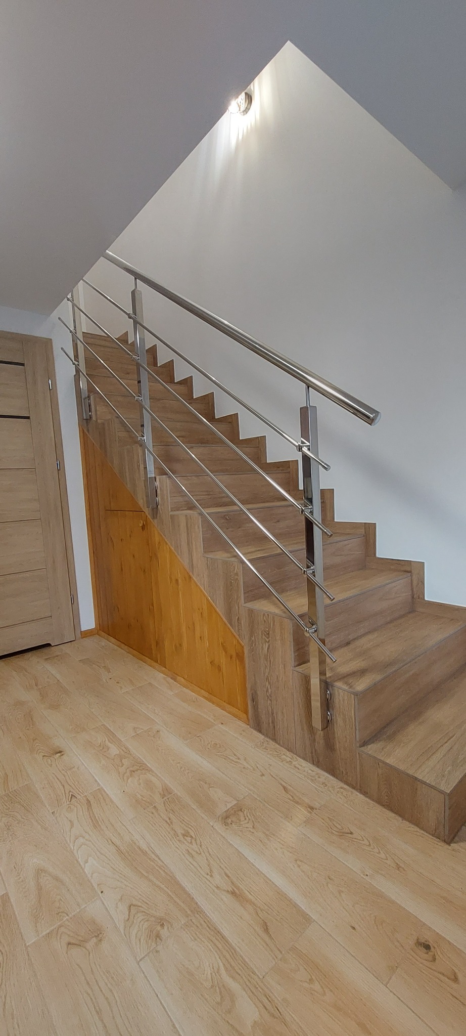 Schody drewniane z prostą, stalową barierką, widok z dołu, oświetlenie sufitowe