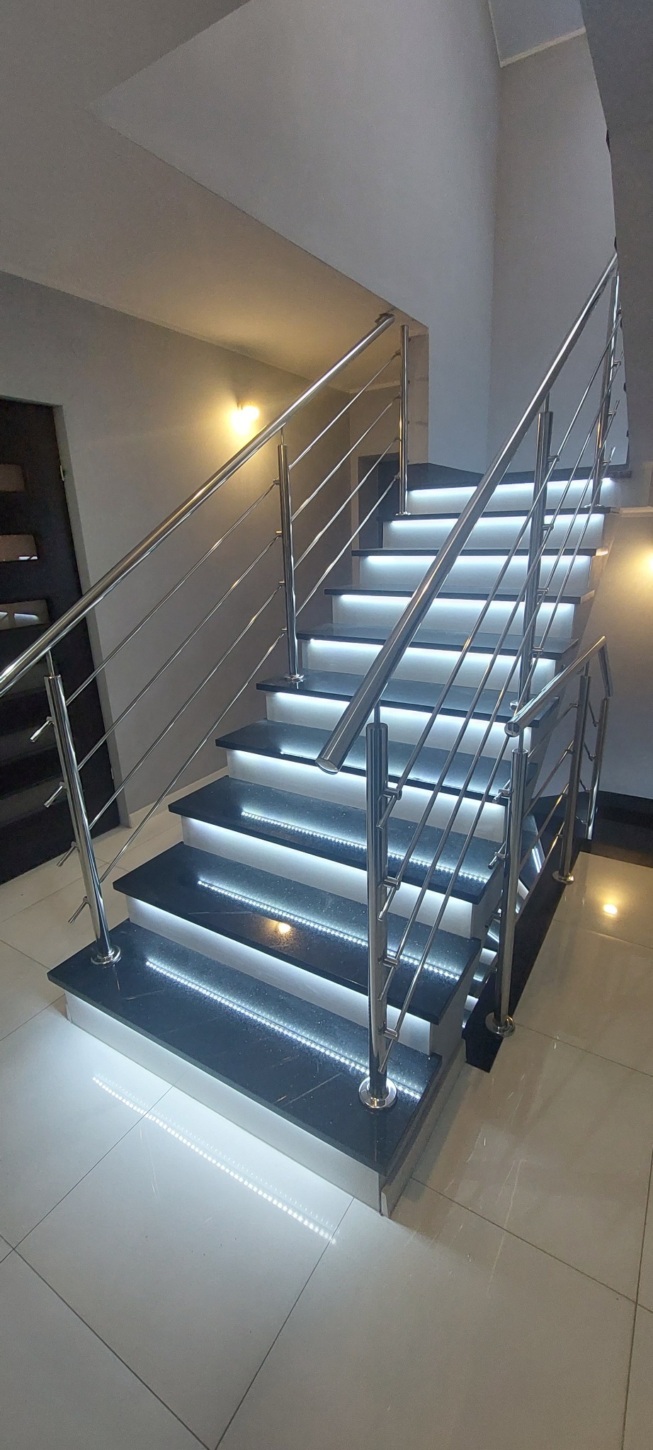 Schody z czarnego kamienia z podświetleniem LED i balustradą ze stali nierdzewnej, widok z dołu, nowoczesny design.