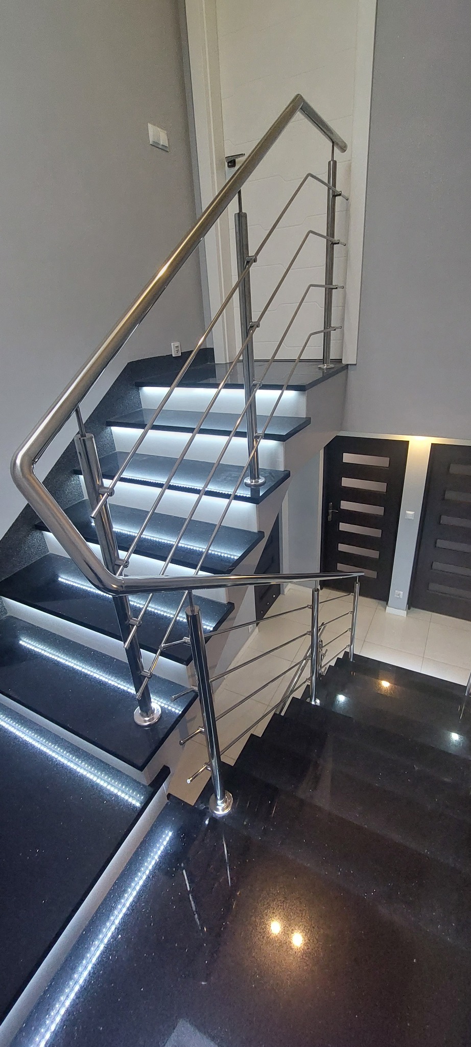 Nowoczesne schody z czarnego kamienia z podświetleniem LED i balustradą ze stali nierdzewnej, widok z góry na dół, minimalistyczny design.