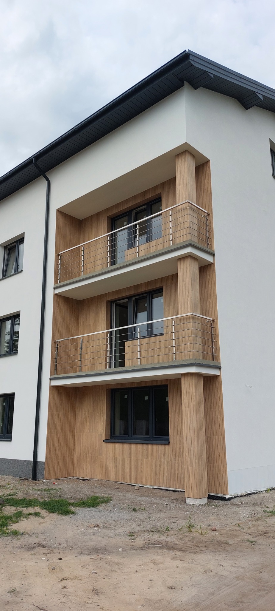 Nowoczesny budynek z trzema balkonami z metalowymi balustradami, wykończony drewnopodobną okładziną.