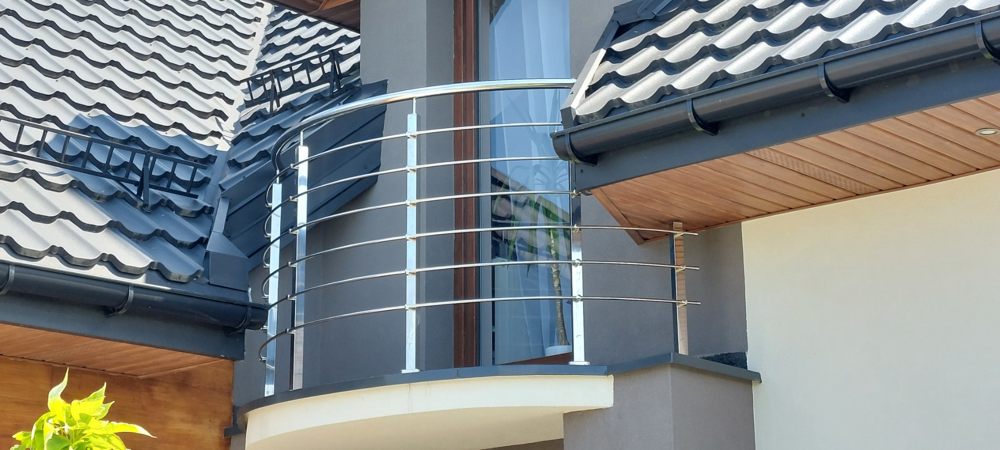 Zaokrąglona, zewnętrzna balustrada ze stali nierdzewnej na balkonie nowoczesnego domu z ciemnoszarą dachówką.