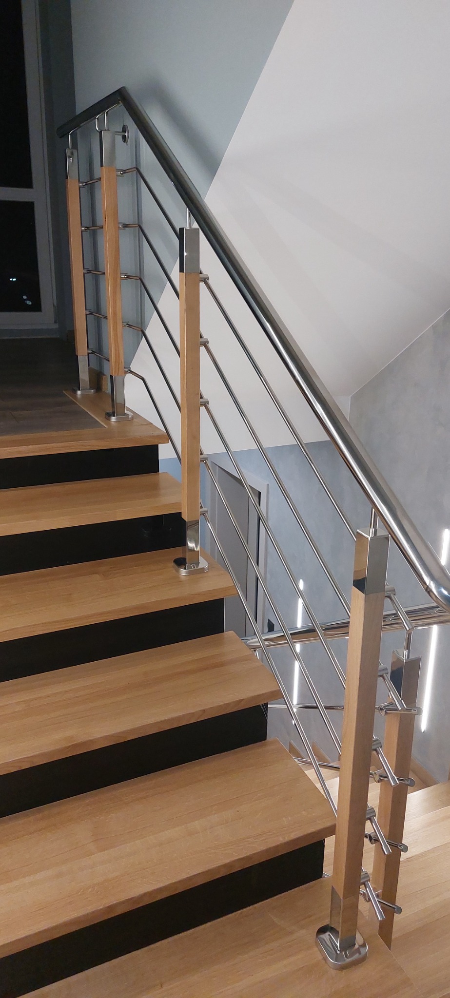 Schody z drewnianymi stopniami i balustradą ze stali nierdzewnej z drewnianymi słupkami, widok z dołu na górę, nowoczesny design.