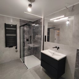 Piotr - Nowoczesna łazienka w szarościach z czarnymi akcentami: kabina prysznicowa typu walk-in, grzejnik drabinkowy, szafka pod umywalkę z czarnymi frontami i baterią, duże lustro z oświetleniem LED.