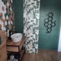 Piotr - Nowoczesna łazienka z zielonymi płytkami, heksagonalnymi wzorami i tropikalnym motywem na ścianie, umywalka nablatowa na drewnianej szafce z czarnym kranem i grzejnik drabinkowy w kształcie plastra...